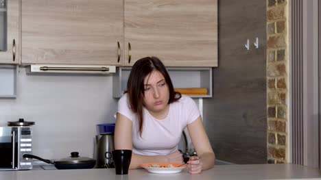 Young-woman,-falling-asleep,-eating-at-the-table-in-the-kitchen
