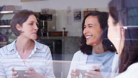 Freundinnen-lachen-im-Coffee-Shop,-gesehen-durch-Fenster