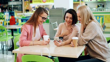 Modern-girls-are-using-smartphone-together-sitting-in-cafe-and-looking-at-screen-then-doing-high-five-and-laughing.-Modern-technology-and-friendship-concept.