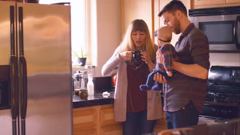 A-young-couple-drinking-their-morning-coffee-in-the-kitchen,-while-the-young-man-holds-their-baby