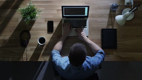 Top-Ansicht-des-männlichen-Programmierers-Schreiben-Code-auf-seinem-Desktop-Computer-bei-Nacht.-Sein-Tisch-wird-von-kaltem-Blaulicht-von-außen-beleuchtet.