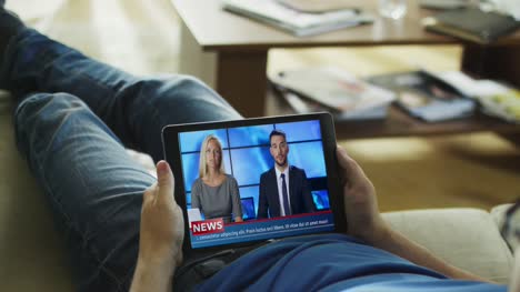 Entspannter-Mann-Lying-auf-His-Couch-Watches-News-Broadcast-auf-seinem-Tablet-Computer.