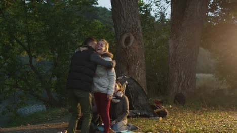 Man-arrives-to-the-campside-where-his-friends-are-sitting-next-to-campfire-and-a-girl-meets-him-with-a-hug.