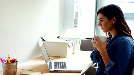 Female-executive-using-laptop-white-having-coffee