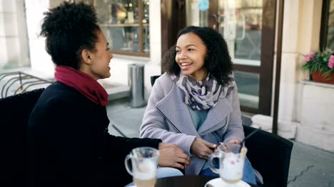 Zwei-attraktive-Mixed-Race-Frauen-im-Straßencafé-sprechen-und-Kaffee-trinken.-Freunde-haben-Spaß-nach-dem-Besuch-Mall-Verkauf