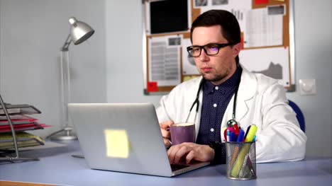 Male-doctor-working-on-his-workplacean-and-have-a-break-to-drink-some-coffee.