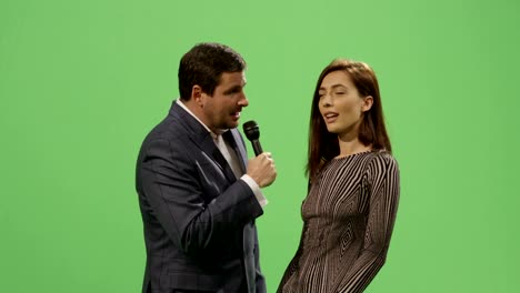 Medien-Reporter-mit-einem-Mikrofon-nimmt-ein-Interview-mit-einer-Frau-in-einem-Kleid-auf-ein-Mock-up-green-Screen-im-Hintergrund.