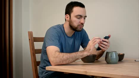 Hombre-joven-con-teléfono-mientras-desayunando
