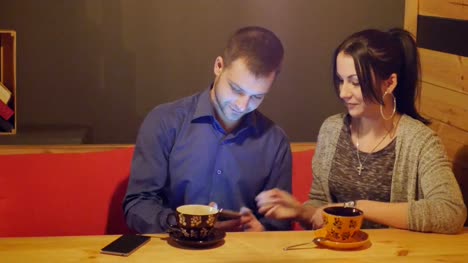 A-couple-sitting-in-a-cafe,-talking,-drinks-coffee-and-watching-the-phone