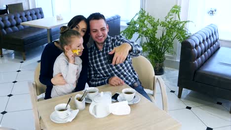 Happy-father-takes-selfie-photo-with-his-wife-and-daughter-during-their-tea-time-in-cafe-or-restaurant
