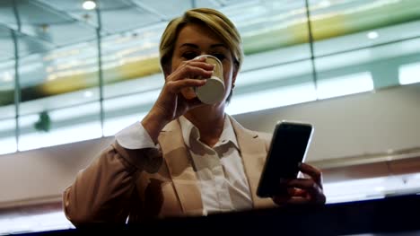 Businesswoman-holding-mobile-phone-and-drinking-coffee