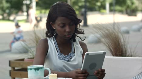 Mujer-de-negocios-joven-africana-trabajando-y-usando-tableta-en-café-al-aire-libre