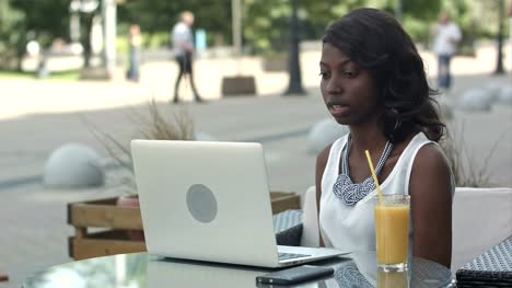 Young-african-woman-sitting-alone-in-a-cafe-having-a-videoconferance-on-a-laptop