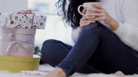 Young-girl-with-cup-sits-on-floor-near-christmas-gifts