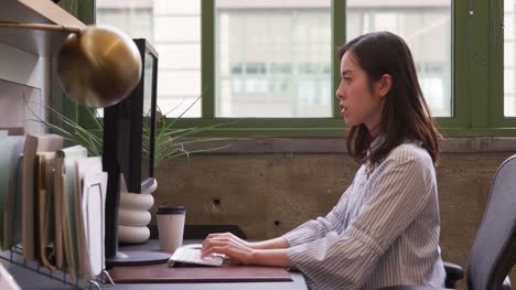Mujer-asiática-joven-usando-la-computadora-en-una-oficina,-vista-lateral