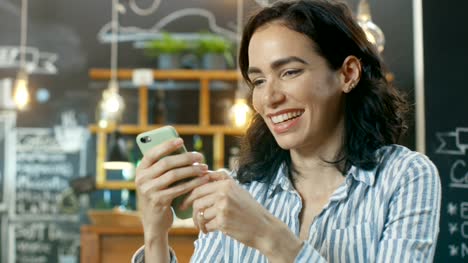 Beautiful-Woman-Uses-Smartphone-while-Sitting-in-the-Cafe.-Background-of-This-Stylish-Coffee-Shop.