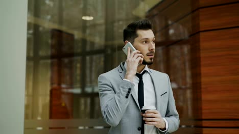 Stedicam-tiro-de-hombre-de-negocios-hablando-con-smartphone-y-caminando-en-el-pasillo-de-la-oficina-moderna