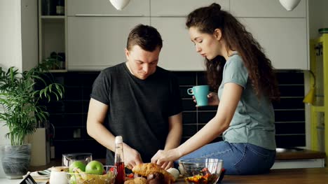 Glückliches-junges-Paar-Kochen-Ameisen-in-der-Küche-zu-Hause-sprechen.-Attraktiver-Mann-seine-Freundin-beim-Schneiden-von-Gemüse-zum-Frühstück-morgens-füttern