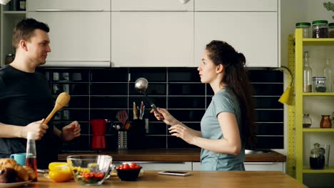 Happy-couple-having-fun-in-the-kitchen-fencing-with-big-spoons-while-cooking-breakfast-at-home