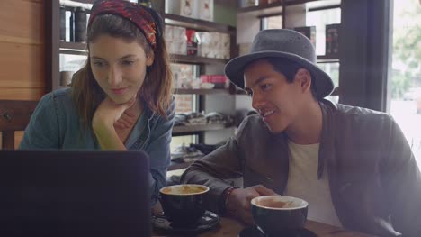 Una-pareja-joven-buscando-un-ordenador-portátil-en-una-cafetería
