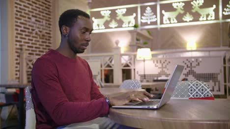 Portrait-of-happy-african-businessman-sitting-in-a-cafe-and-working-on-laptop