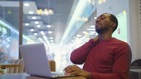 Retrato-de-feliz-empresario-africano-sentado-en-un-café-y-trabajando-en-ordenador-portátil