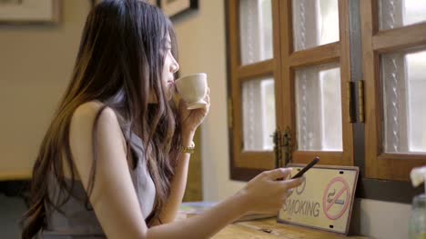 Asiatische-Frauen-Telefon-spielen-und-trinken-heißen-Kaffee-in-Coffee-Shop.