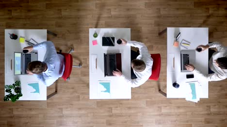 Drei-junge-Unternehmer-arbeiten-auf-Laptops,-trinken-Kaffee-gleichzeitig-arbeiten,-Konzept,-Bürokonzept,-Kommunikationskonzept,-Top-shot