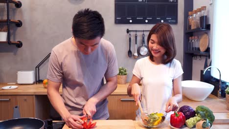 Man-hands-cutting-tomato-in-the-kitchen.-Beautiful-happy-asian-couple-are-cooking-in-the-kitchen.-Young-asian-couple-have-romantic-time-while-staying-at-home.-Couple-lifestyle-at-home-concept.