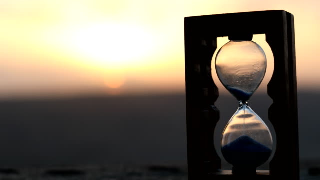 Hourglass-Passing-of-Time-Lapse-Clouds.-An-hourglass-in-front-of-a-bright-blue-sky-with-puffy-white-clouds-passing.-Time-concept.-Sunset-time.-Selective-focus