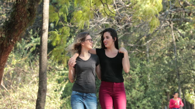 Zwei-Freundinnen-zusammen-zu-Fuß-in-den-Park,-umarmen-einander-lachen