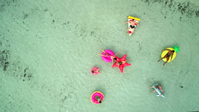 Aerial-view-of-friends-floating-on-inflatable-mattresses-in-transparent-sea.