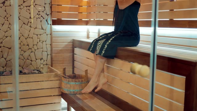 Girl-is-sitting-in-a-sauna-on-a-wooden-bench-with-bare-feet.-Girl-relaxes.-Span-camera-bottom-up.
