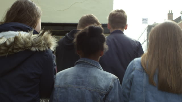 Rear-View-Of-Teenagers-Walking-Along-Street-Shot-On-R3D