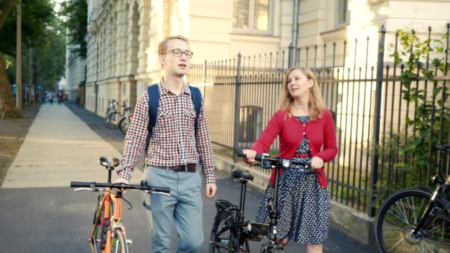 feliz-pareja-joven/esposos-con-bicicletas,-caminar-y-hablar-en-un-día-soleado-en-la-ciudad-de-la-calle
