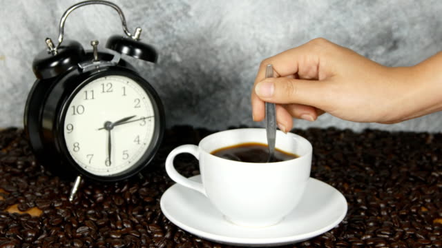 4k-Nahaufnahme-weibliche-Hand-rühren-Cup-schwarz-Kaffee---weibliche-Hand-mit-Löffel-um-zu-rühren,-frischem-Boden-schwarz-weiße-Kaffeetasse-Untertasse-neben-Kaffee-in-Bohnen,-Kaffee-Zeit