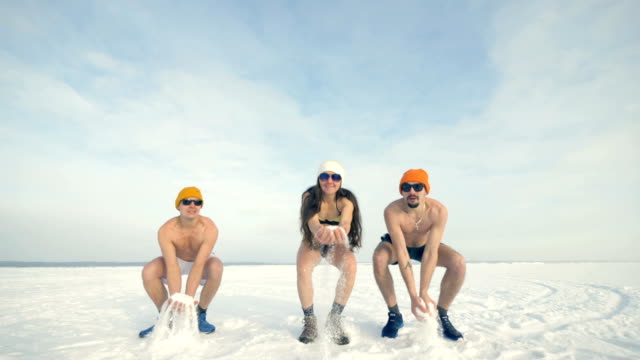 Drei-Freunde-spielen-mit-Winterschnee-beim-Badeanzüge-tragen.