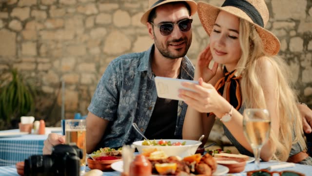 Junge-Touristen-entspannen-am-Restaurant-mit-mediterraner-Küche-und-Blick-auf-smartphone
