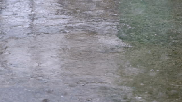Regentropfen-fallen-auf-dem-Bürgersteig-bilden-eine-Pfütze
