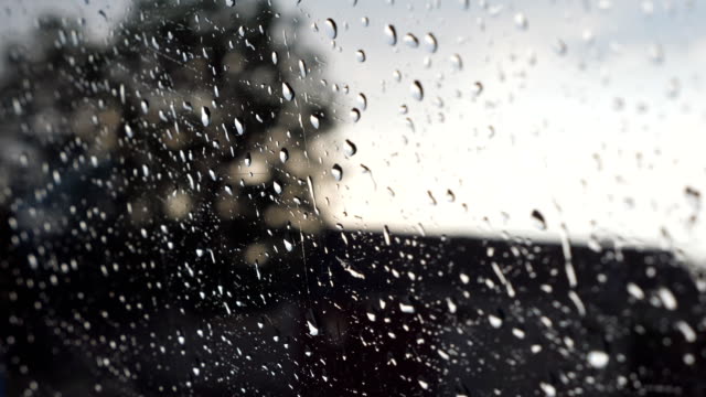 Close-up-of-raindrops-on-car-window-during-bad-weather-with-blur-background.-Water-droplets-fall-on-the-glass-of-automobile-during-drive-at-countryside.-POV-Slow-motion