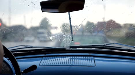Punto-de-vista-desde-el-asiento-delantero-para-parabrisas-de-coche-retro-viejo-durante-mal-tiempo.-Limpiadores-de-quitar-las-gotas-de-lluvia-desde-la-ventana-del-automóvil-vintage-durante-el-estar-parado-en-un-atasco-de-tráfico.-Cerrar-lenta