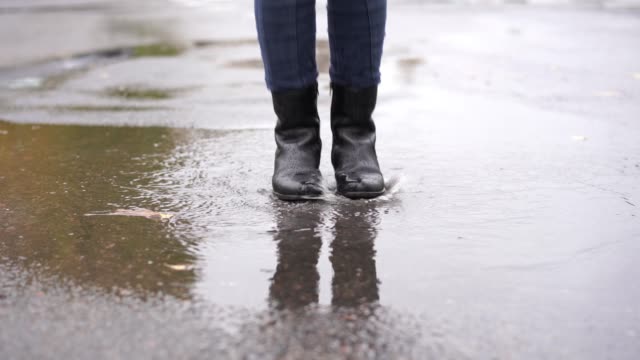 eine-Mädchen-in-schwarzen-Lederstiefeln-stolpert-in-die-herbstliche-Pfütze-während-des-Regens