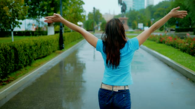Happy-and-beautiful-red-haired-woman-walking-in-the-park-under-the-pouring-summer-rainю-View-from-the-back