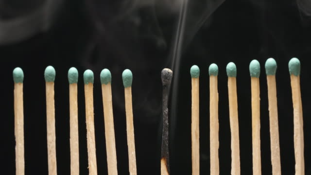 SLOW-MOTION:-Smoke-of-single-burned-matchstick-between-row-of-new-matchsticks