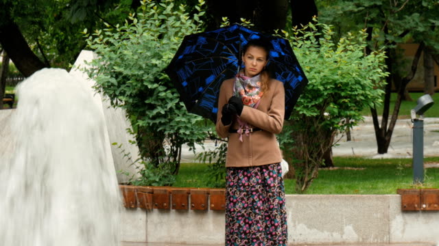 A-beautiful-girl-with-sad-eyes-is-standing-in-the-rain-in-the-city-park,-near-the-fountain.