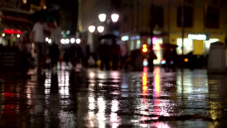 Abstract-background-rainy-late-evening-in-the-city-in-naturale-dark-tones.-Raindrops-fall-on-the-colorful-asphalt-illuminated-by-street-lamps.-Among-the-crowd-of-pedestrians-go-two-friends-under-umbrellas-and-talk.-Lifestyle-of-modern-city
