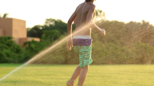 Young-boy-child-playing-in-the-lawn-with-water-sprinkles-in-slow-motion-60fps-and-in-4k-resolution.-Uninhibited-infancy-enjoying-the-small-things-in-life-during-sunset-golden-hour-time-in-green-field-of-idealic-moment