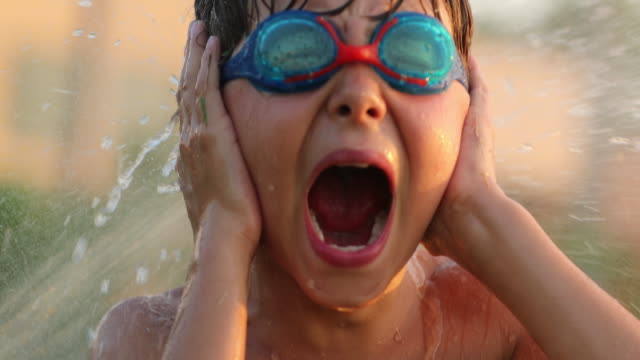 Child-screaming-covering-ears-with-hands.-4k-resolution-of-child-yelling-from-the-top-of-his-lungs-while-water-sprinkles-spray-him-with-water-in-60fps-slow-motion