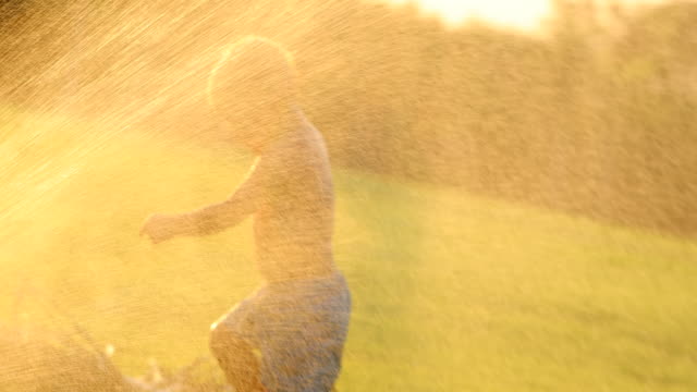 Dreamy-60fps-slow-motion-scene-of-infant-baby-boy-having-fun-with-water-sprinkles-during-sunset-golden-hour-time-in-4k-clip-resolution.-Baby-enjoying-the-simple-things-in-life-in-4K
