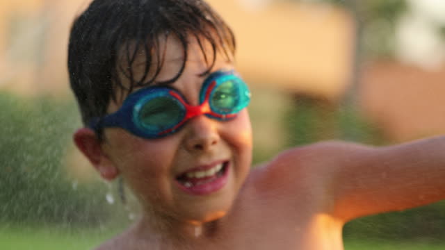 Glückliches-Kind-lächelt-Kamera-während-besprüht-mit-Wasser-besprengt-in-60fps-4k-Auflösung.-Positive-aussehendes-Kind-lächelnd-zu-Kamera-während-der-Zeit-des-Sonnenuntergangs-Sommer-Ferien-Urlaub-4k.mov
